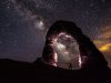 person standing under a rock formation on a starry night