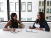 two woman in black sits on chair near table